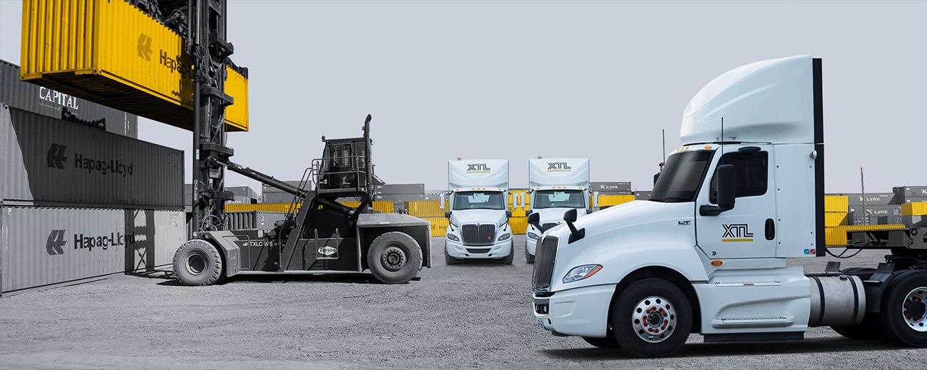 Photo of a shipping yard with a XTL truck in the foreground and shipping containers in the background.